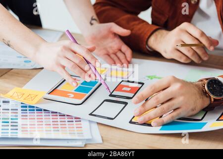 Vista ritagliata dei progettisti che pianificano la progettazione dell'esperienza utente di un sito Web mobile con framework sulla tabella isolati in grigio Foto Stock