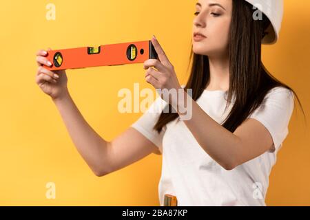 vista ritagliata della donna di mano concentrata che tiene la livella di spirito su sfondo giallo Foto Stock