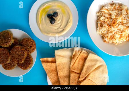 Famosa cucina tradizionale araba, mediorientale, israeliana. Salsa tahini, pane pita, riso con vermicelli e falafel su fondo blu. Disposizione piatta Foto Stock