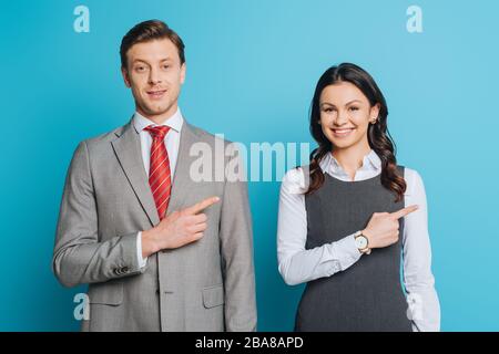 allegro uomo d'affari e donna d'affari puntando con le dita mentre sorridendo alla macchina fotografica su sfondo blu Foto Stock