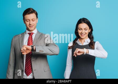 uomo d'affari sorridente e donna d'affari guardando orologi da polso su sfondo blu Foto Stock