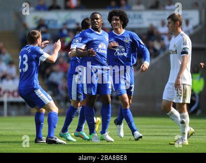 Victor Anichebe (al centro) di Everton celebra dopo aver segnato con i suoi compagni di squadra mentre ben Davies (a destra) di Swansea City guarda su dejected Foto Stock