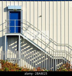 Scala in metallo attaccata al lato dell'edificio che porta alla porta blu al primo piano di un moderno magazzino Foto Stock