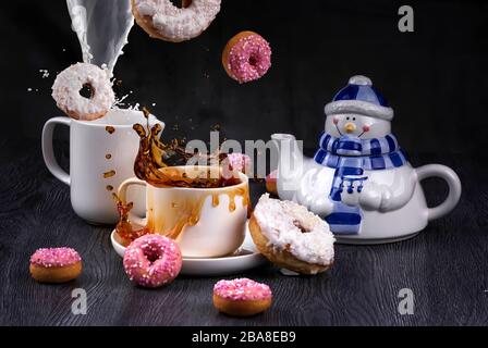 Divertente teiera con spruzzi e gocce di tè caldo e ciambelle glassate rosa. Prima colazione di Natale. Gravità zero Foto Stock