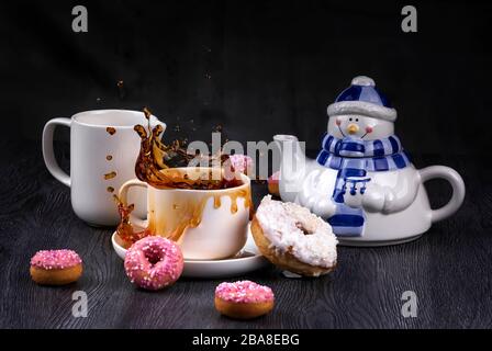 Divertente teiera con spruzzi e gocce di tè caldo e ciambelle glassate rosa. Prima colazione di Natale. Gravità zero Foto Stock