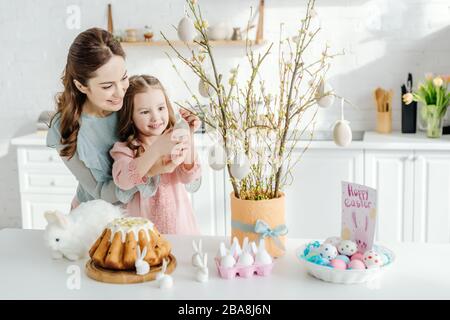 felice capretto che tocca l'uovo decorativo di pasqua sul ramo del salice vicino alla madre Foto Stock