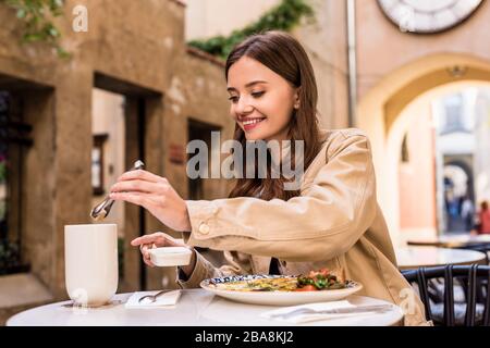 Il fuoco selettivo della donna che mette il cubo dello zucchero nella tazza del tè nel caffè in città Foto Stock