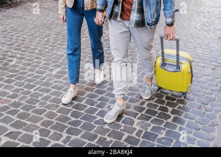 Vista tagliata della coppia che tiene le mani e viaggia insieme con la valigia Foto Stock