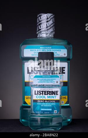 Piccolo flacone di collutorio Listerine davanti a un grande contenitore non aperto. Studio di basso scatto di prodotto di igiene orale su uno sfondo scuro. Foto Stock