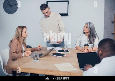 l'attenzione selettiva dei colleghi multiculturali che lavorano sulla carta e dell'uomo afro-americano che utilizza il laptop sullo sfondo Foto Stock