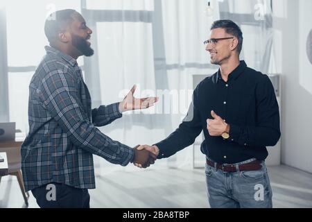 sorridendo colleghi multiculturali che scuotono la mano e si mostrano come Foto Stock