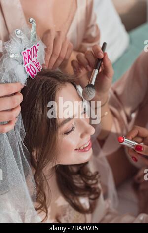 Vista tagliata delle donne multiculturali che mettono il trucco con spazzola cosmetica e rossetto sulla sposa alla festa della bachelorette Foto Stock