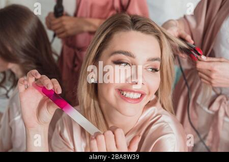 Fuoco selettivo della ragazza bionda che tiene la lima del chiodo e sorridente con gli amici multiculturali al partito del bachelorette Foto Stock