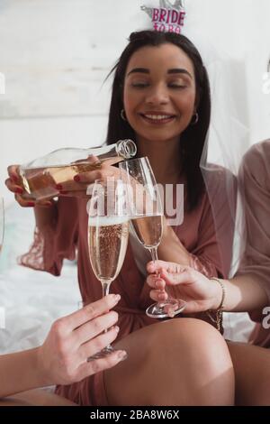 Vista tagliata della sposa afro-americana che versa champagne in bicchieri con gli amici al bachelorette party Foto Stock