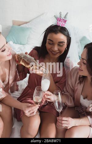 Vista ad alta angolazione della sposa afro-americana che versa champagne in bicchieri con gli amici al bachelorette party Foto Stock