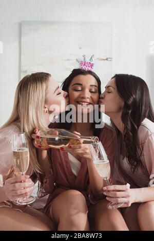 Sposa afro-americana che versa champagne in bicchieri e baci da amici a bachelorette party Foto Stock