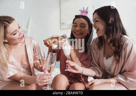 Sposa afro-americana che versa champagne in bicchieri con gli amici alla festa di bachelorette Foto Stock