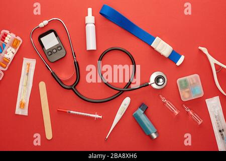 Vista dall'alto di stetoscopio, inalatore per asma, medicinali e oggetti medici su sfondo rosso Foto Stock