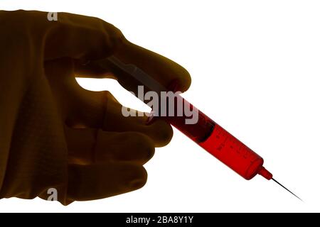 Siringa con liquido rosso tenuto in mano con i guanti. Primo piano immagine della silhouette retroilluminata isolata su sfondo bianco. Messa a fuoco selettiva. Foto Stock