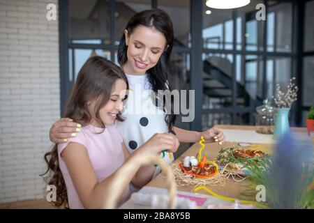 Mamma abbracciando le sue figlie spalla con tenerezza e sorridente Foto Stock