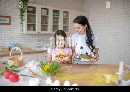 Mamma e figlia che tengono conigli pasquali fatti in casa e cercando contented Foto Stock