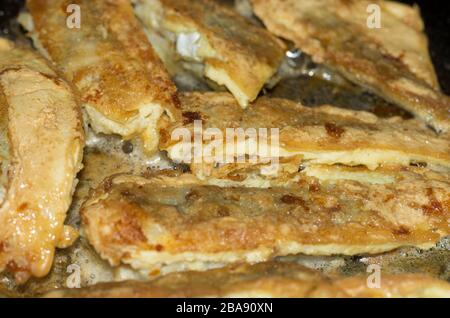Fritto in pastella a fette di Northern Whiting in una padella con olio Foto Stock