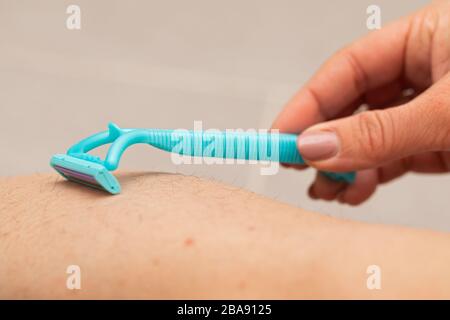 Immagine ravvicinata della donna che tiene il rasoio, rasando la gamba pelosa con folliculite Foto Stock