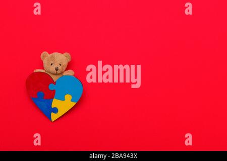 Colorful Puzzle forma del cuore e Teddy su sfondo rosso. World Autism consapevolezza, concetto. Foto Stock