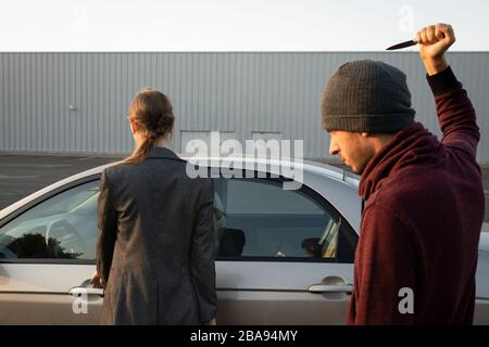 Un uomo armato di un coltello ha attaccato una donna indifesa in un parcheggio vicino a un supermercato. Vuole rubare tutti i suoi soldi e una macchina. Foto Stock