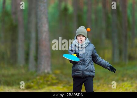 Ragazzino con maschera a causa del virus corona giocare a tennis nel parco. Quarantena del coronavirus Foto Stock