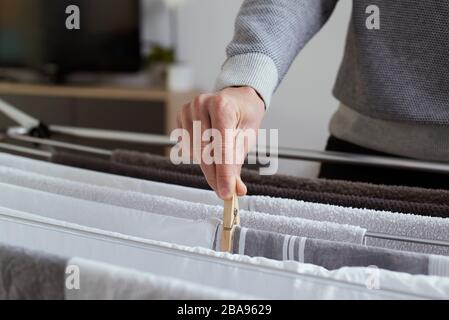 primo piano di un giovane caucasico appeso abiti bagnati su una rastrelliera di asciugatura nel soggiorno o nella stanza della famiglia della sua casa Foto Stock