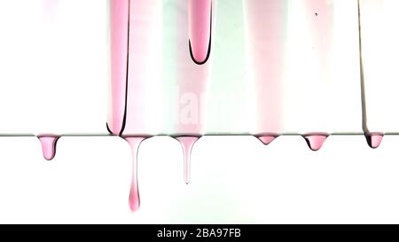 Gocciolamento lento di goccioline di liquido rosso trasparente. Foto Stock