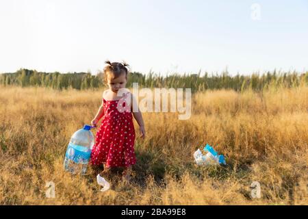 La bambina raccoglie i rifiuti sparsi nella foresta. La bambina raccoglie i rifiuti sparsi nella foresta. Il bambino lotta per un ambiente pulito. Foto Stock