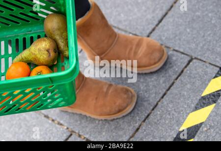 Monaco, Germania. 26 marzo 2020. Una donna attende con un carrello della spesa in un mercato settimanale ad una base della frutta e della verdura in una coda dietro un contrassegno che indica la distanza permessa alla persona seguente. Per ridurre il rischio di infezione con il coronavirus, le persone dovrebbero mantenere la loro distanza l'una dall'altra. Credit: Sven Hoppe/dpa/Alamy Live News Foto Stock