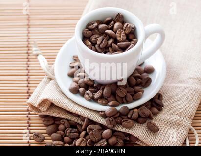 Chicchi di caffè in tazza su sacchetto di lino e tappetino di bambù Foto Stock