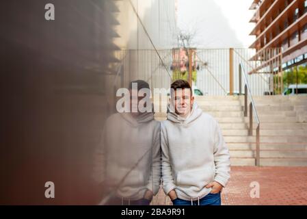 Ritratto di giovane maschio con le mani in tasca appoggiata a parete all'esterno Foto Stock