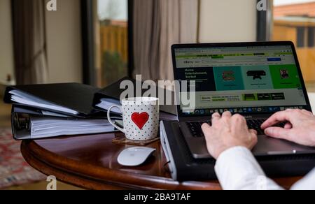 Donna che lavora su un laptop sul tavolo a casa con schermo che mostra la pagina di eBay online shopping sito web Foto Stock