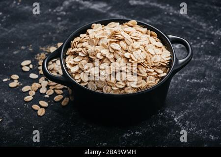 Vista dall'alto di una ciotola nera con fiocchi d'avena su sfondo nero. Concetto di cibo sano. Foto Stock