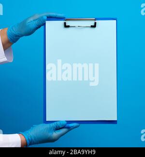 le mani del medico femminile in guanti blu di lattice medico tiene una piegatrice con una graffetta, luogo per scrivere una diagnosi, messaggio Foto Stock