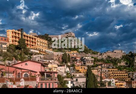Bella vista del centro abitato della città collinare di Taormina, Messina, Sicilia, Italia, contro un cielo drammatico Foto Stock