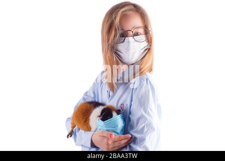 Giovane ragazza carina in una maschera medica e occhiali sta tenendo porcellino d'India in una maschera protettiva nelle sue mani contro sfondo grigio chiaro, copia spazio. Pre Foto Stock