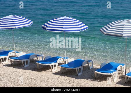 Ombrelloni e sedie a sdraio blu per il relax in località di mare. Vacanze estive e viaggi per il mare. Servizio a pagamento su spiagge confortevoli. Foto Stock