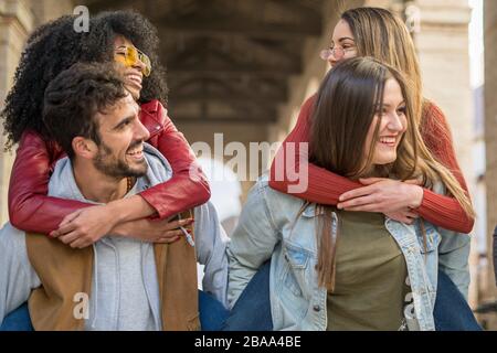 Giovani amici che giocano e si divertono insieme piggybacking. Studenti di culture diverse che comunicano insieme. Integrazione di gare diverse e. Foto Stock