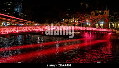 Il ponte Cavenaugh, la sola sospensione ponte sul fiume Singapore, illuminato in rosso la notte. Foto Stock