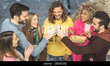 Un gruppo di giovani si trova in strada nel centro città. Fanno tostare le scale, bevono birre e mangiano cibo di strada (tagliatelle). Foto Stock