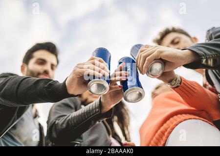 I giovani amici tostano con birre in scatola. Mettere a fuoco la lattina, i volti sfocati. Foto Stock