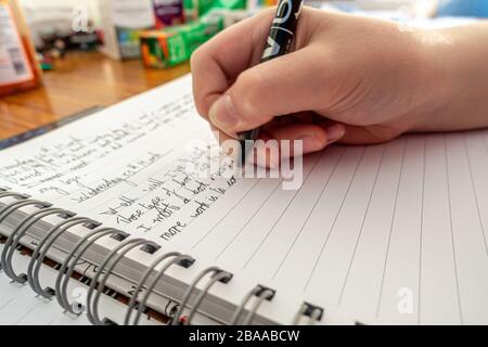 Un giovane ragazzo scrive un diario degli eventi durante il blocco del coronavirus come pratica di scrittura e per ricordare gli eventi attuali nel futuro. Foto Stock