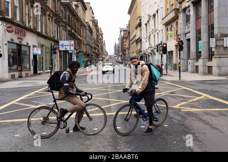 Glasgow, Scozia, Regno Unito. 26 marzo 2020. Vista dal centro della città di Glasgow il giovedì durante il terzo giorno del governo ha sancito il blocco Covid-19. La città è in gran parte deserta. Sono aperti solo negozi di alimentari e minimarket. Nella foto, due ciclisti deliveroo si fermerono per un ritratto .Iain Masterton/Alamy Live News Foto Stock