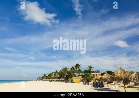 Splendida vista sulla spiaggia di sabbia bianca di Aruba. Lettini blu sotto ombrelloni su acqua turchese e cielo blu con sfondo bianco nuvole. Caraibi. At Foto Stock