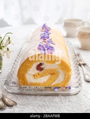 Rotolo svizzero ripieno di panna montata e fragole, decorato con piante commestibili selvatiche - veronica e viola morto-ortica Foto Stock